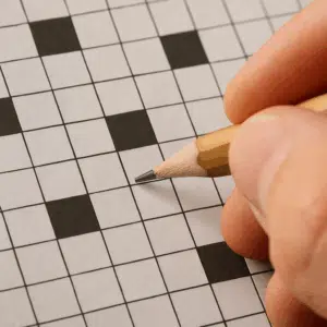 Close-up af krydsordsopgave med ’Belgisk by’ som clue og en hånd, der skriver med blyant.