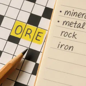 Nærbillede af krydsord med markeret ord 'malm', blyant og noter med synonymer og løsninger.