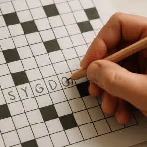 Hånd med blyant udfylder krydsordcelle med ordet sygdom på papir